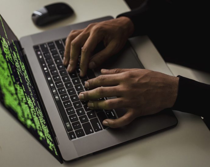 From above of crop anonymous male hacker typing on netbook with data on screen while sitting at desk