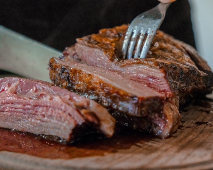 person slicing a meat on brown wooden board