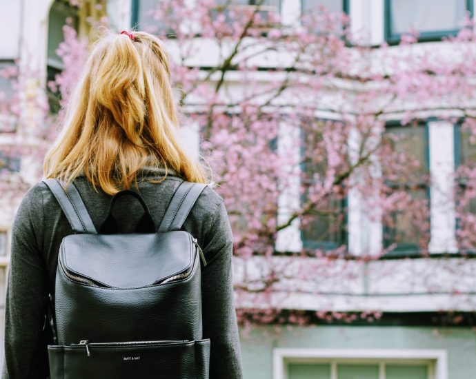 woman wearing backpack facing concrete building