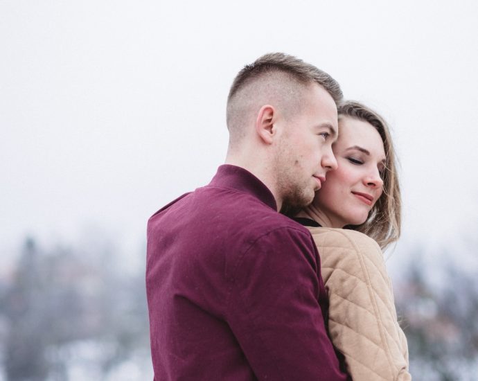 man hugging woman while standing on snowy weather