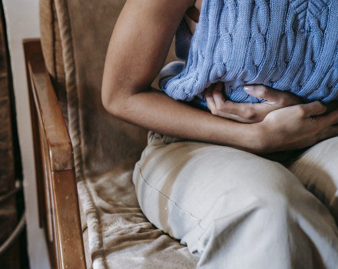 Crop unrecognizable female touching belly while having acute pain in stomach sitting on couch