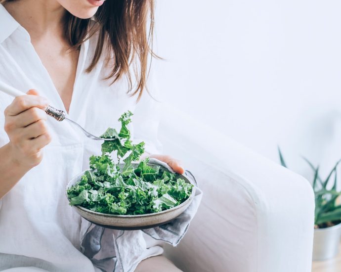 woman in white dress holding silver fork and knife slicing green vegetable on white ceramic bowl