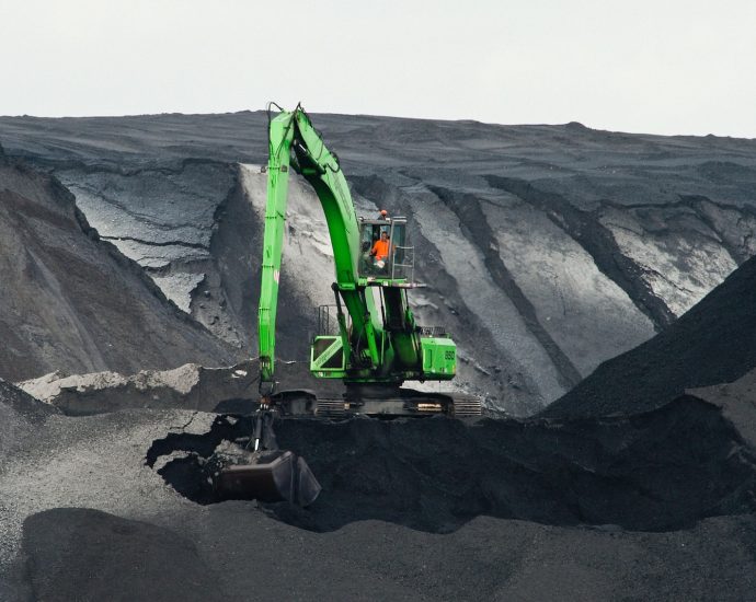 green backhoe digging hole in the middle of mountain