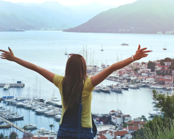 Woman Raising Her Hands Facing Cityscape Near Body of Water