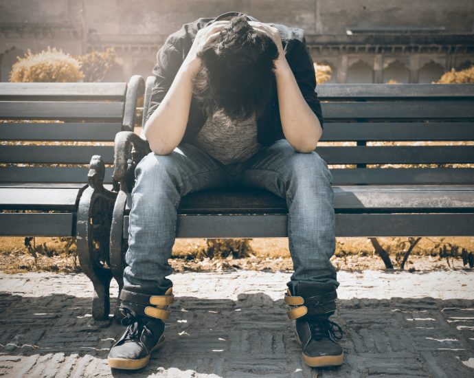 Man in Black Shirt and Gray Denim Pants Sitting on Gray Padded Bench