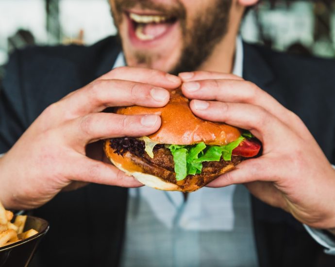 person holding burger bun with vegetables and meat