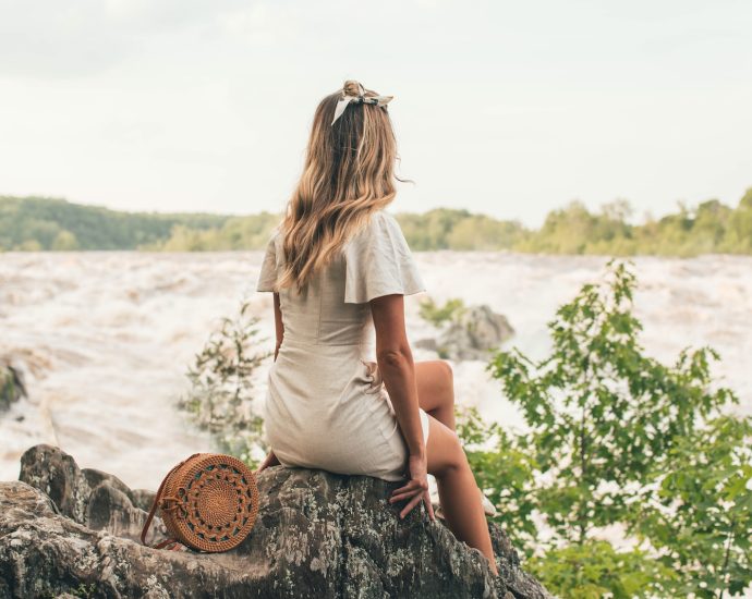 woman sitting on rock beside body of water