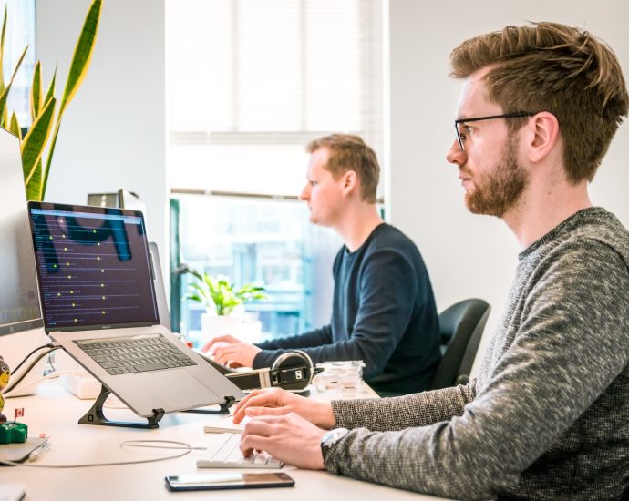 man sitting on chair wearing gray crew-neck long-sleeved shirt using Apple Magic Keyboard