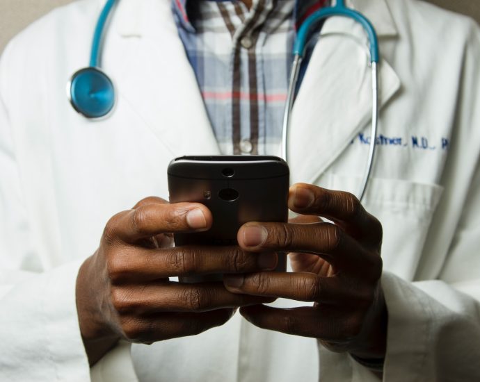 person wearing lavatory gown with green stethoscope on neck using phone while standing