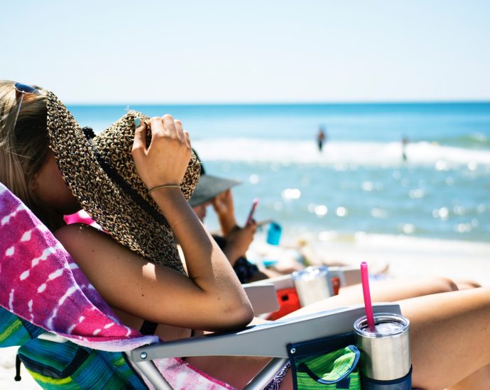 woman lying on sun lounger covering her face with straw hat near sea