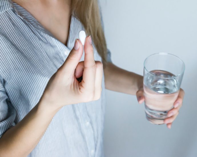 Woman Holding Half-full Glass and White Medicine Pill