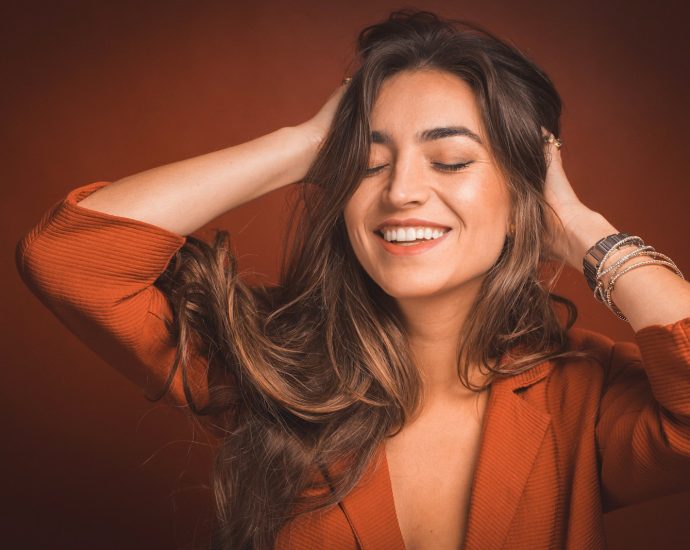 smiling woman in brown top holding hairs