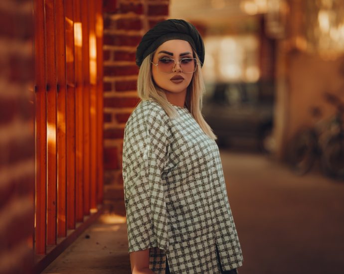 a woman wearing sunglasses and a hat standing in front of a brick wall