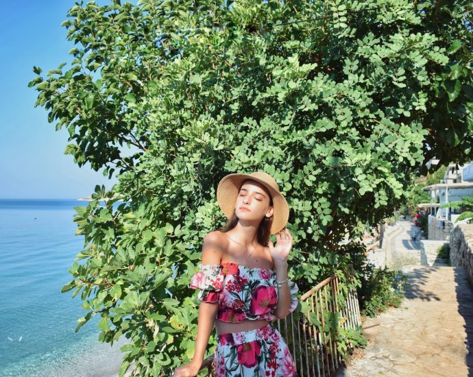 a woman in a floral dress and hat standing next to a tree