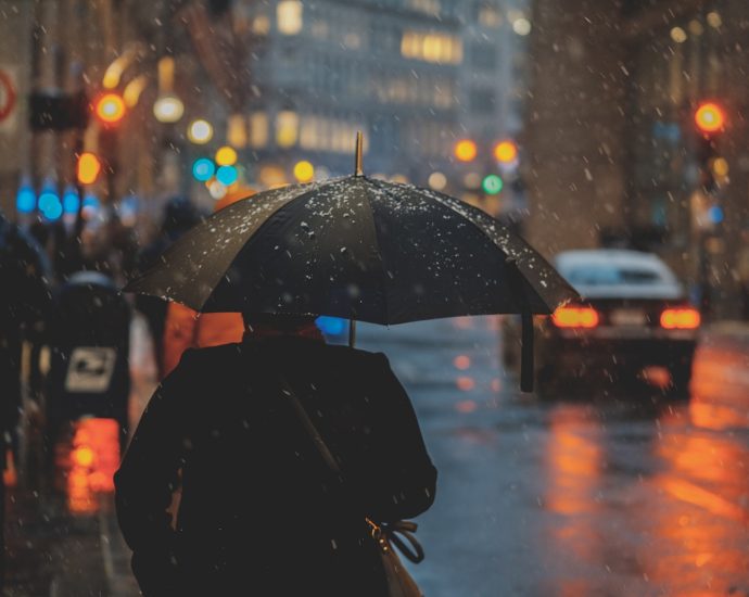 person walking on street and holding umbrella while raining with vehicle nearby