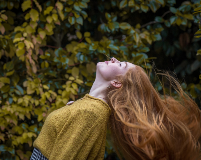 woman wearing brown crew-neck shirt standing in front of green leaves