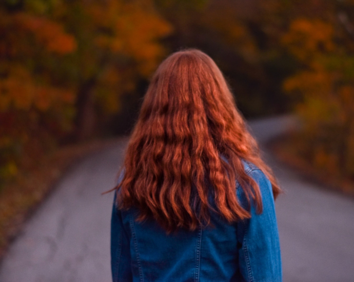 woman in denim jacket walking on empty road