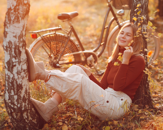 woman in brown long sleeve shirt and white pants sitting on brown dried leaves