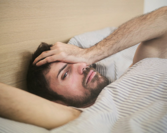 From above of sleepy bearded man just awakened rubbing eyes while lying on bed at home