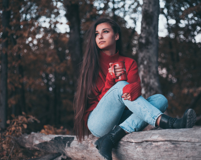 woman in red jacket and blue denim jeans sitting on brown wooden log