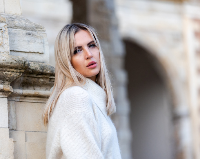 woman in white sweater standing near white concrete wall during daytime