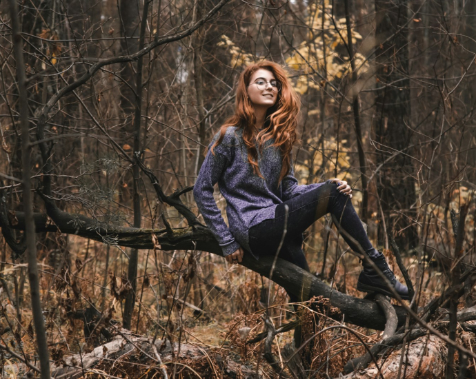 woman in gray and purple sweatshirt sitting on tree truck in forest during daytime