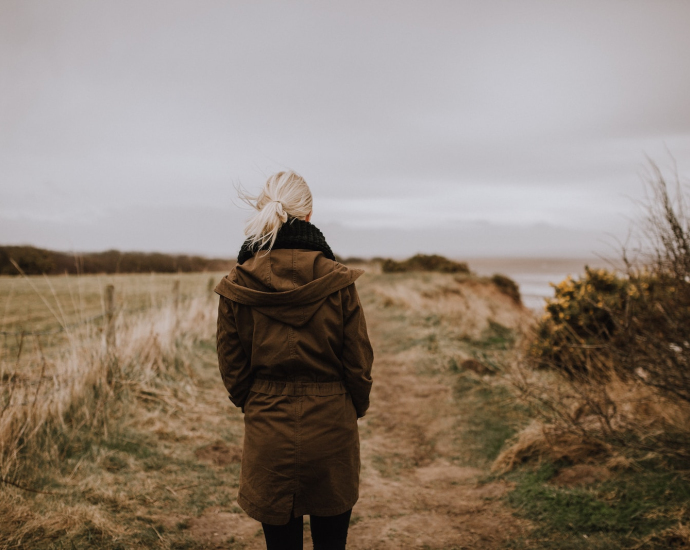 woman in brown coat walking on brown grass