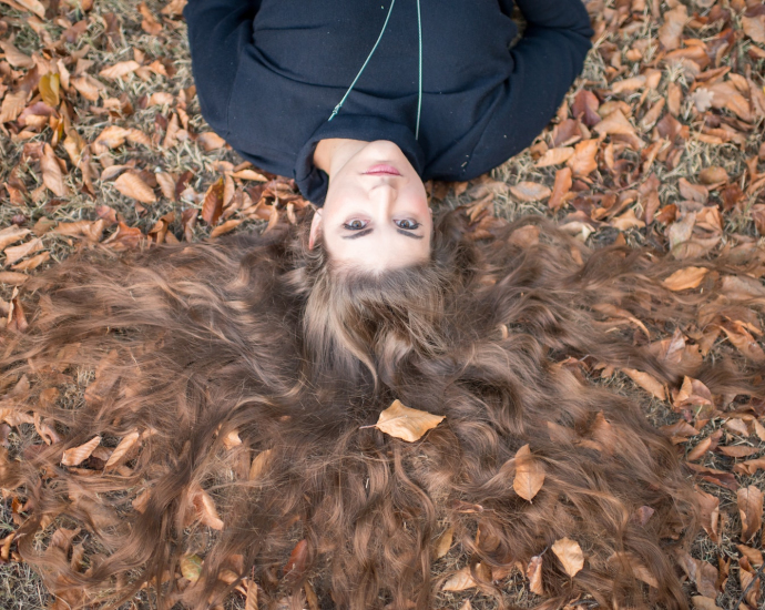 flay lay photography of brown long-haired woman wearing black crew-neck top laying on field with dry leaves