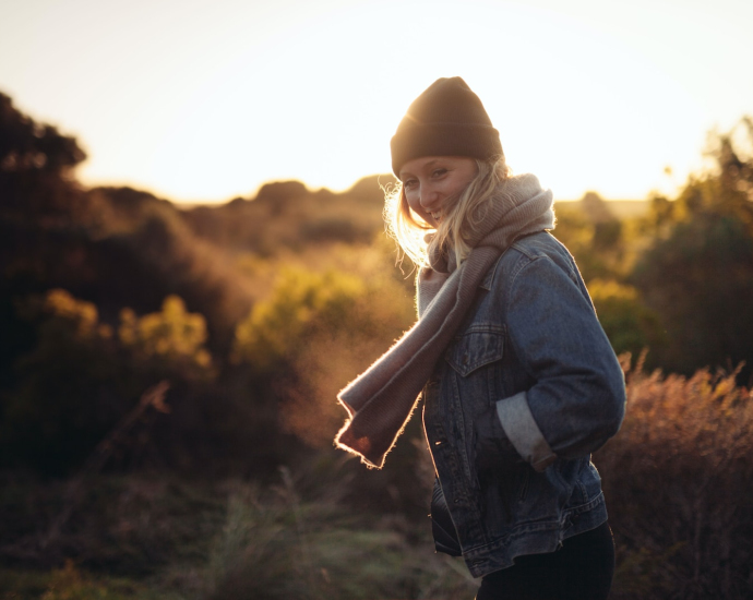 smiling woman taking photo near trees and brown grass during sunrise