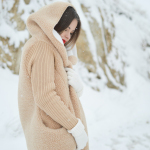 woman in brown corduroy hooded coat standing near brown boulder covered on snow at daytime