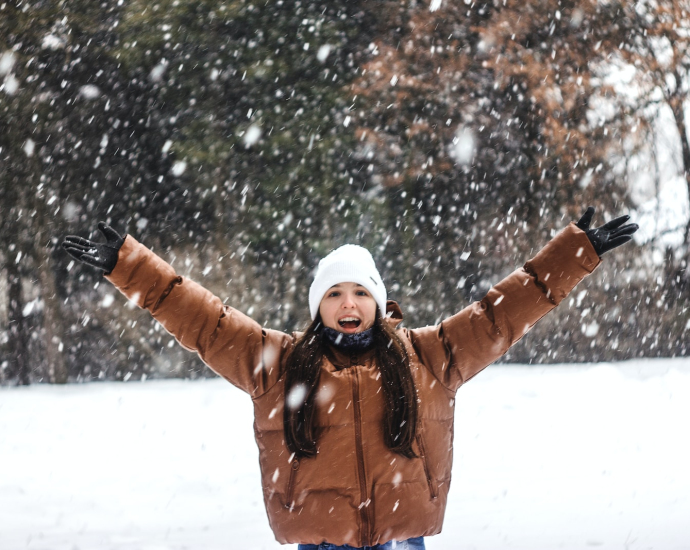 woman in brown jacket and white knit cap standing on snow covered ground during daytime