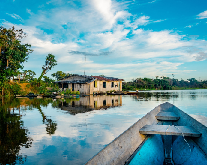 house near blue body of water surrounded with green trees under white and blue sky