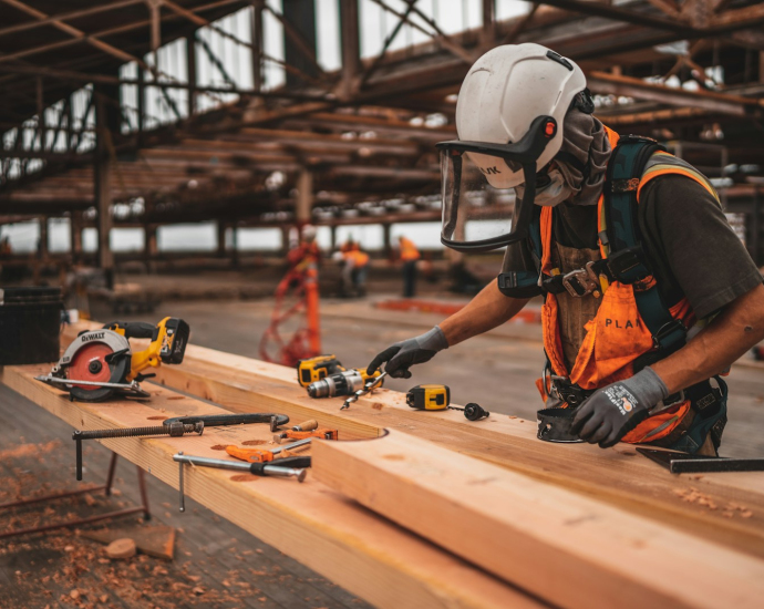 man in orange and black vest wearing white helmet holding yellow and black power tool