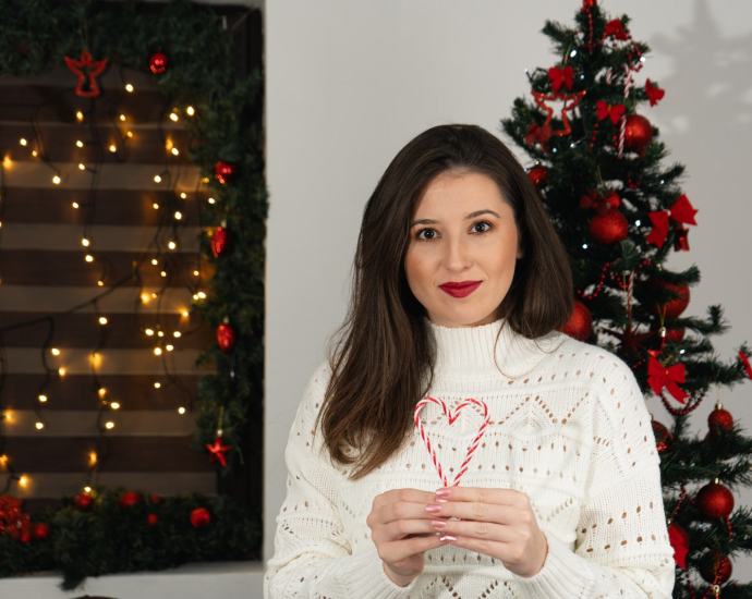 a woman in a white sweater holding a candy cane in front of a christmas tree