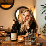 a woman sitting at a table with a bottle of wine