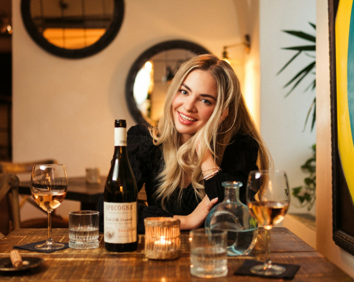 a woman sitting at a table with a bottle of wine