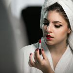 a woman with a towel on her head is putting lipstick on her face