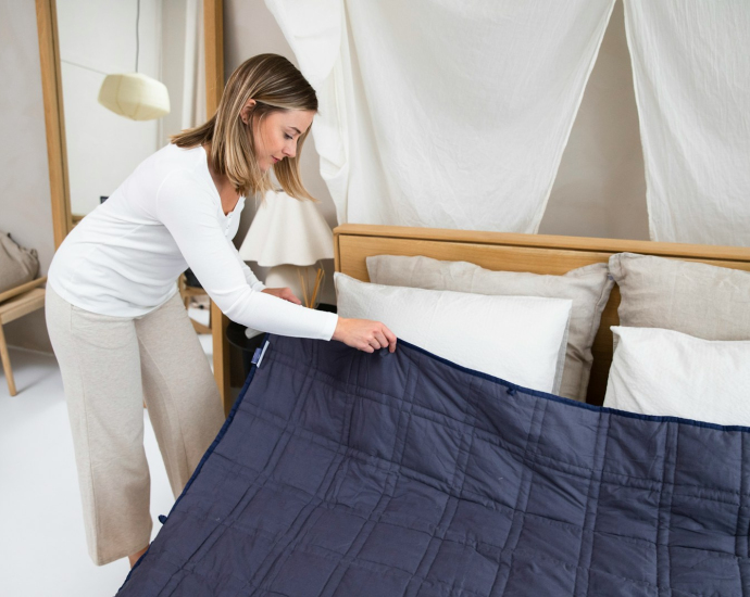 a woman putting a blue blanket on top of a bed