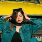 a woman with her head in her hands standing next to a yellow car