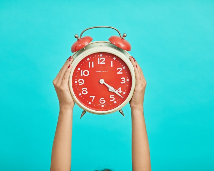 person holding red and beige twin bell analog alarm clock