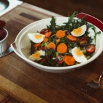 bowl of salad with slide of cooked egg with grapes on the side