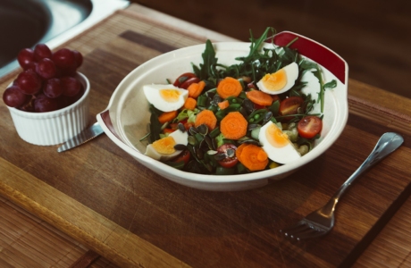 bowl of salad with slide of cooked egg with grapes on the side