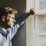 person near clear glass window pane and window blinds low-light photography