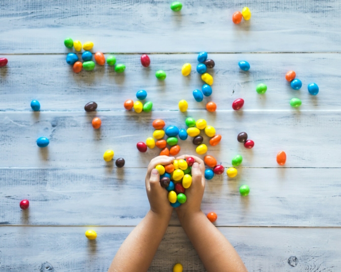 selective photo of kid holding candies on gray wooden pallet board