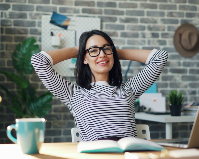 a woman sitting at a desk with her hands behind her head