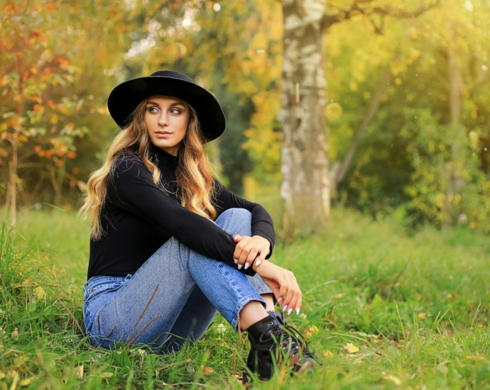 a woman sitting in the grass wearing a black hat