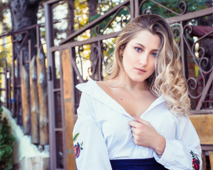 woman in white top standing beside brown metal fene