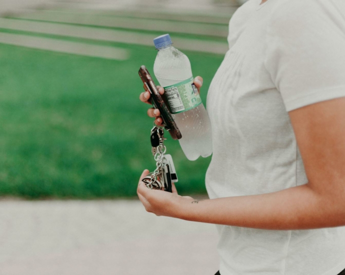 Person Holding Car Keys and Bottled Water