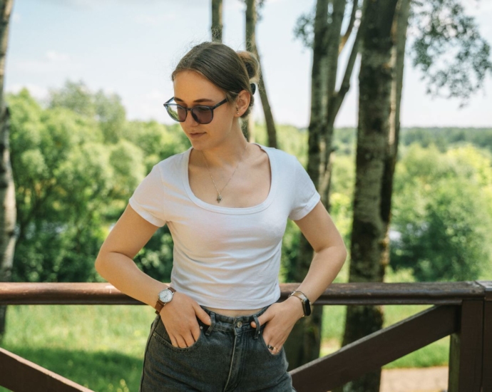 A woman in sunglasses and a white shirt is standing on a wooden deck