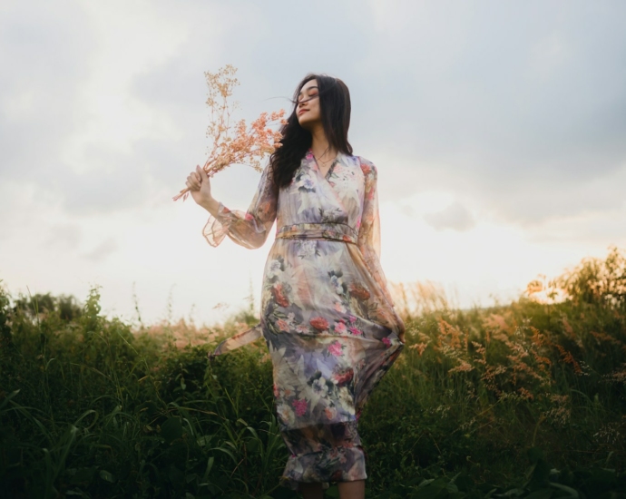 a woman standing in a field holding a bouquet of flowers